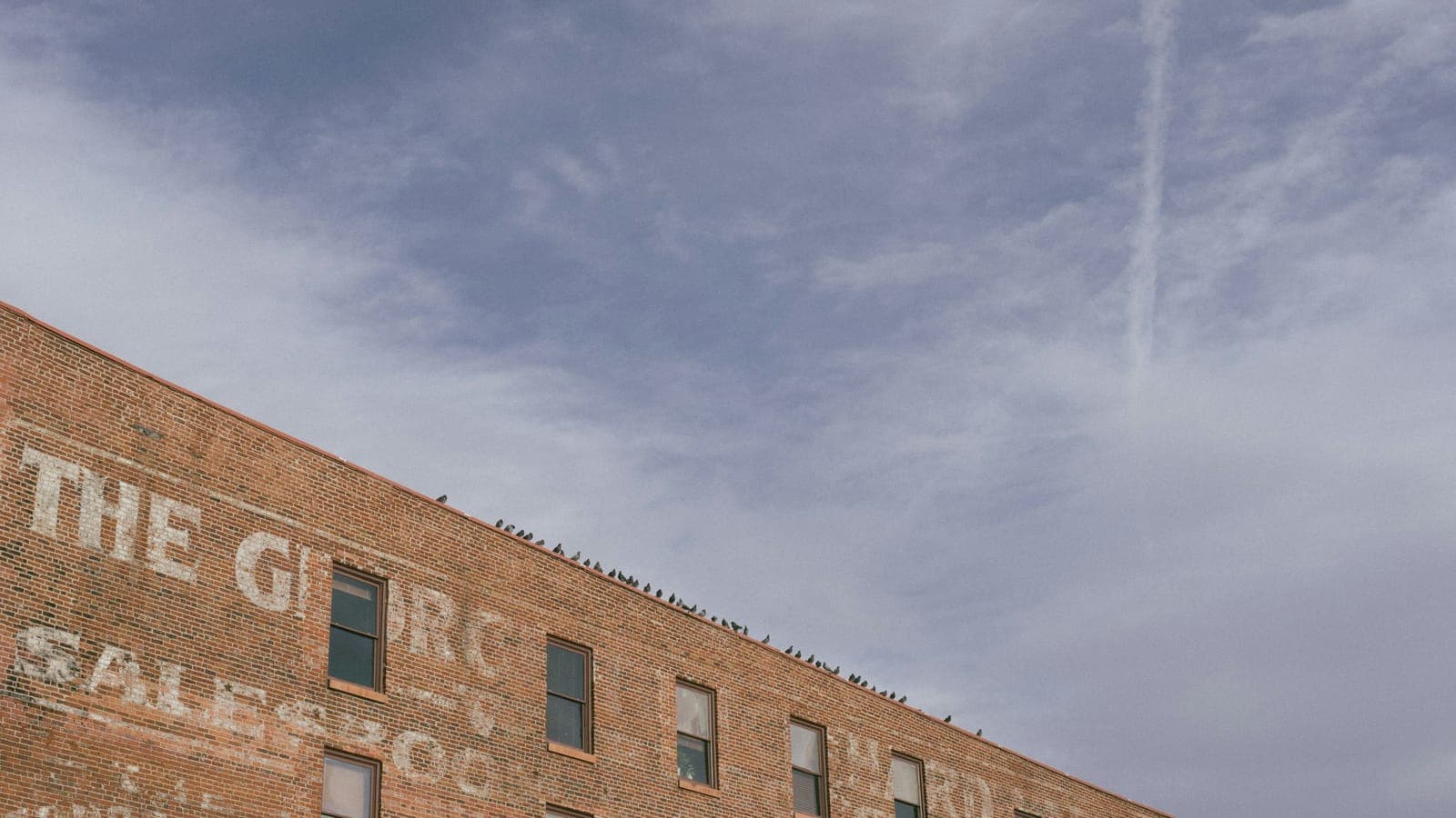 Young professionals walking past brick lofts and rooftop bars in Denver's LoDo neighborhood with the downtown skyline behind them